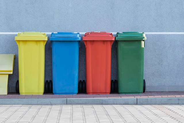 yellow, blue, red, and green garbage bins against a blue wall